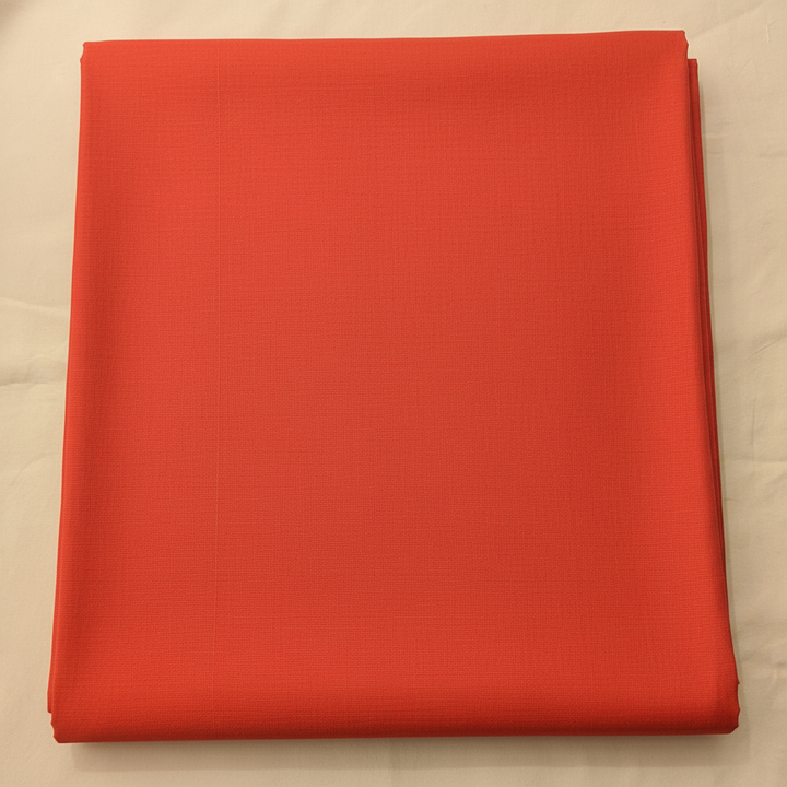 Close-up of the peach-coral cotton saree showing its warm vermilion body and subtle woven texture