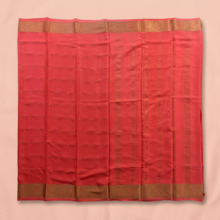 Upstraight overhead view of a coral red pure Mysore crepe silk saree with subtle gold butta motifs and coppery gold woven border bands