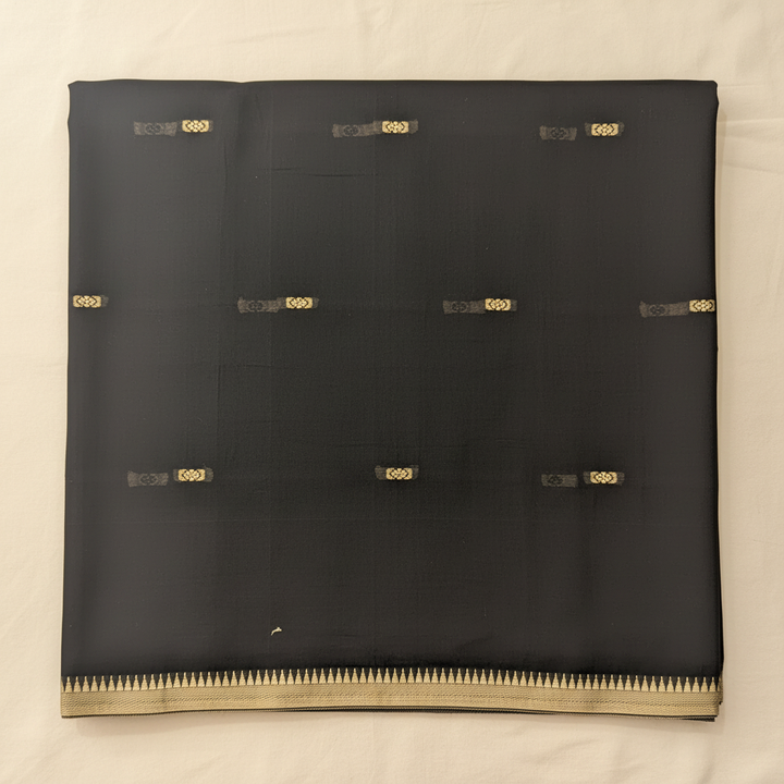 Close-up of the charcoal-black and graphite cotton saree showing its subtle woven texture and scattered antique-gold motifs