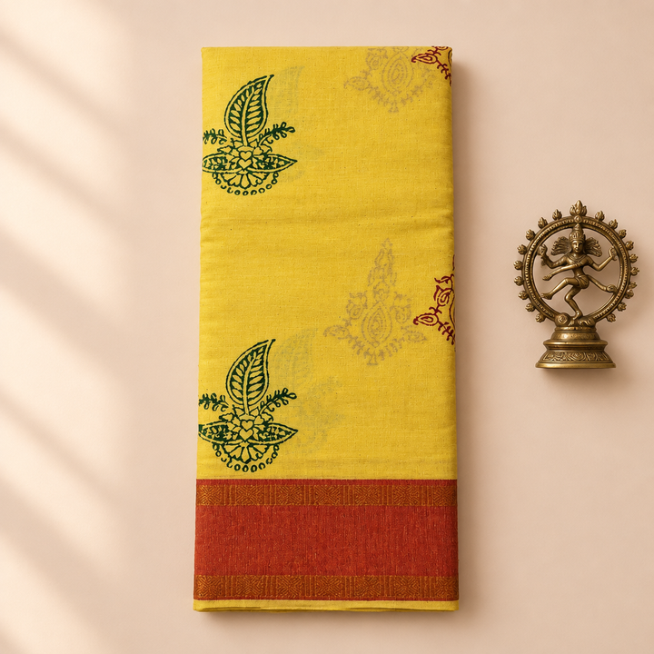 Pale yellow cotton dance saree with floral print and rust-red border, folded flat lay with Nataraja prop