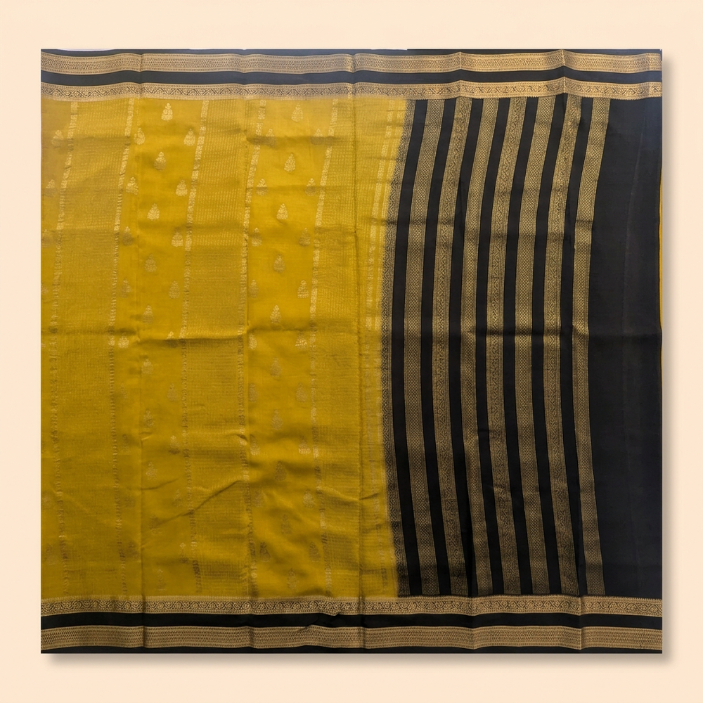 Upstraight overhead view of a mustard yellow and black pure Mysore crepe silk saree with gold butta motifs and black zari-banded contrast section