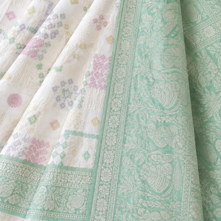 Close-up of the white saree's mint green woven pallu and border with fine self-tone patterns