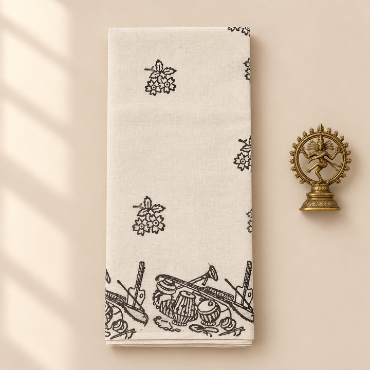 Cream cotton dance saree with black musical instrument print border, folded flat lay with Nataraja prop